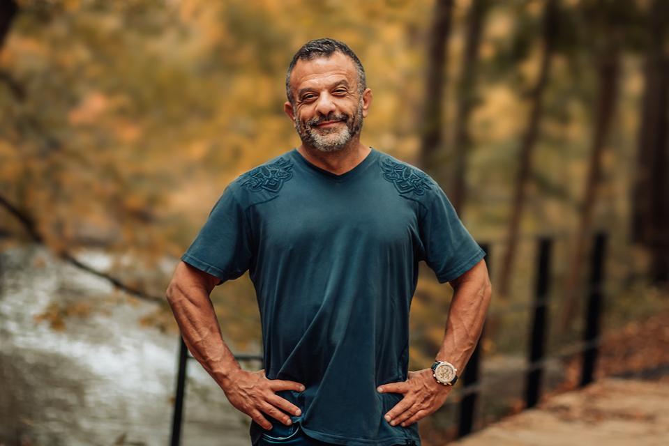 Portrait of middle-aged man smiling in blue-tree t-shirt in the woods.
