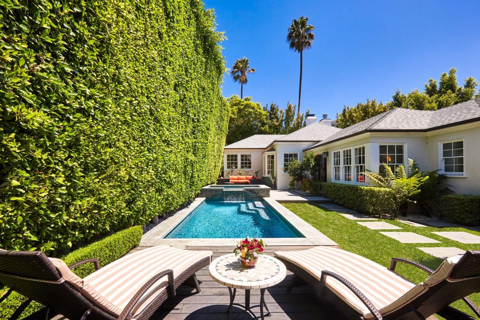 Deck chairs sit in the foreground of a swimming pool and traditional-style home.