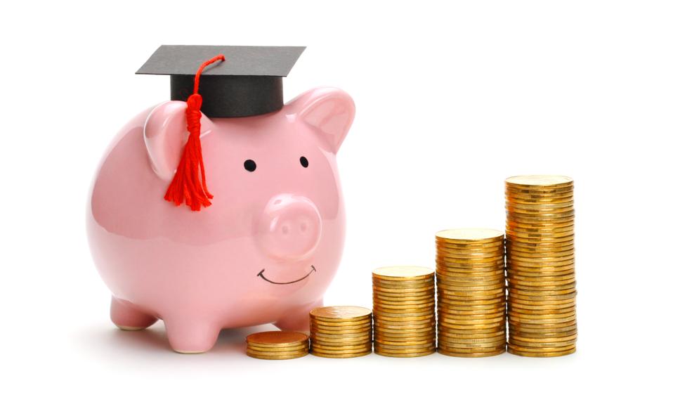 Piggy bank in graduate cap near stack of coins