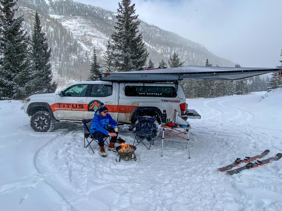 A man warms himself at a portable fire outside his mobile ski lodge.