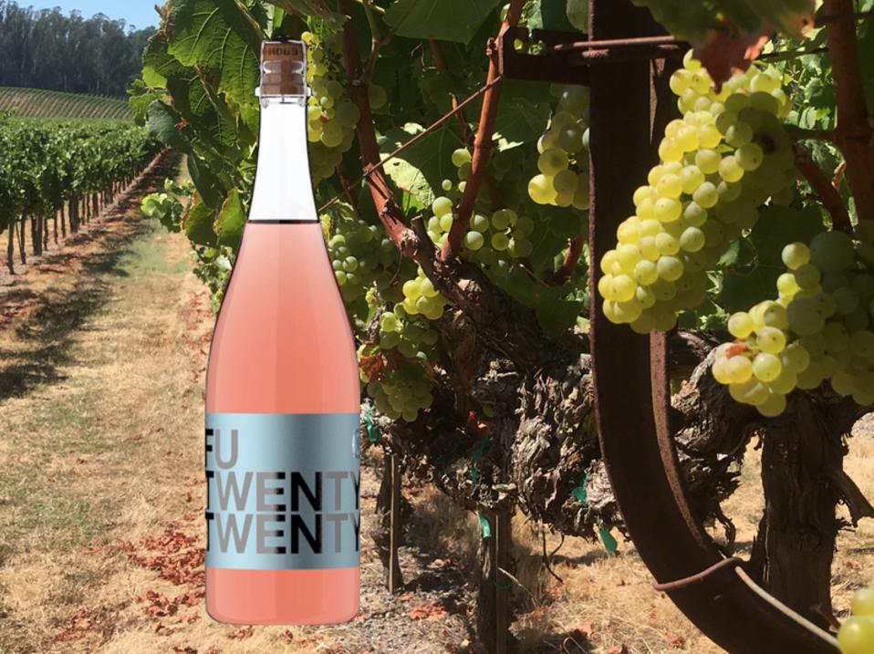 a bottle of pink rose wine sits in front of a row of white grapes