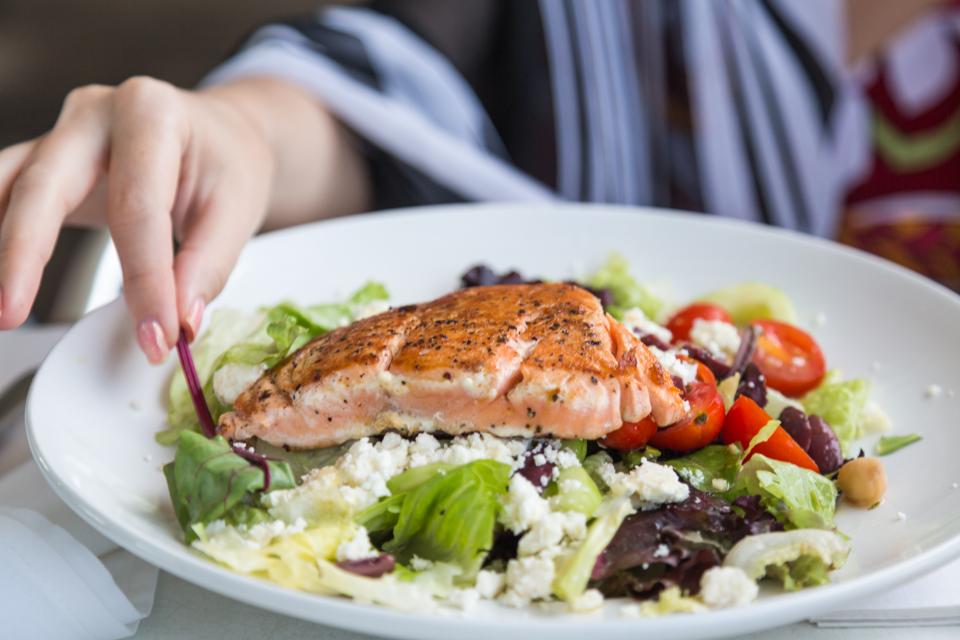 A person eating a salmon fillet on top of a salad.
