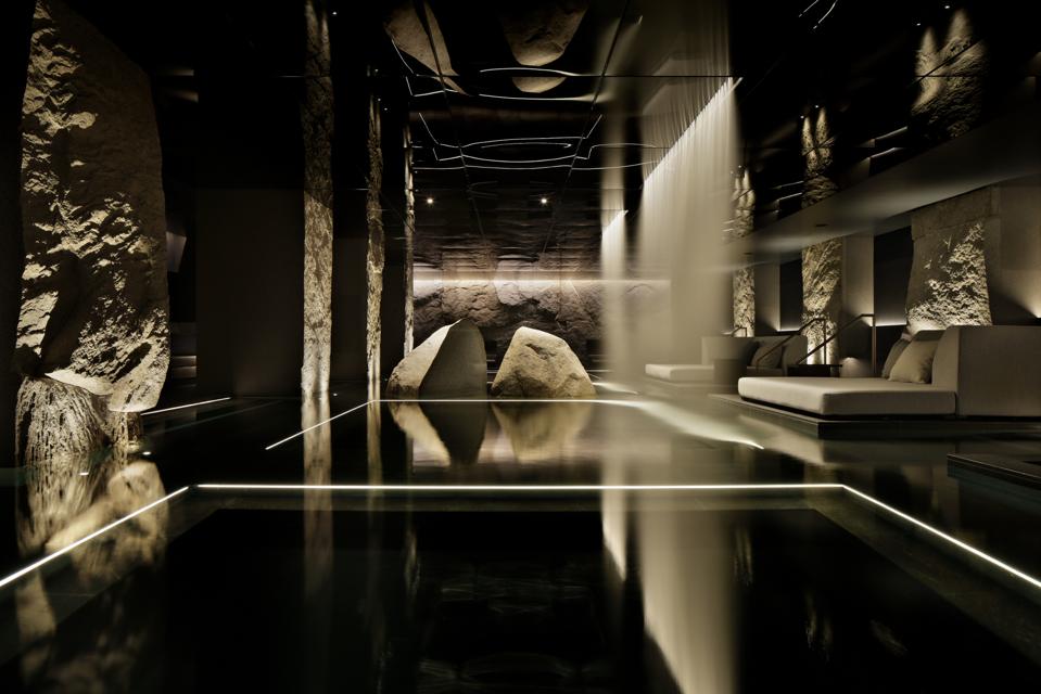 A sleek pool edged by stone walls with a waterfall and dark, moody lighting