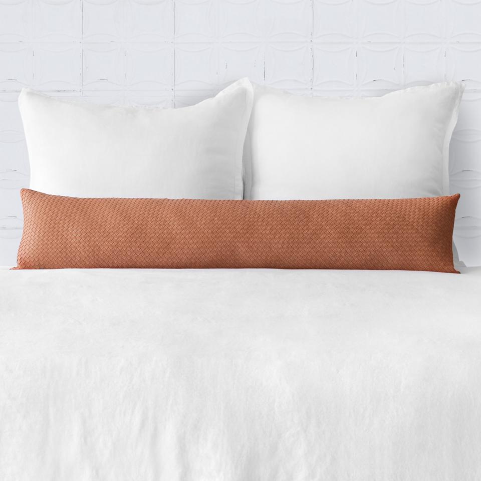 A long woven leather pillow on a bed.