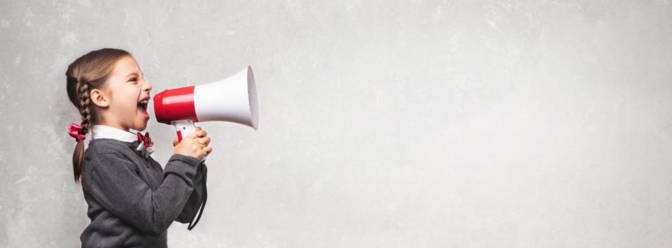 Child Girl Student Shouting Through Megaphone on Grey Backdrop with Available Copy Space. Back to School Concept.