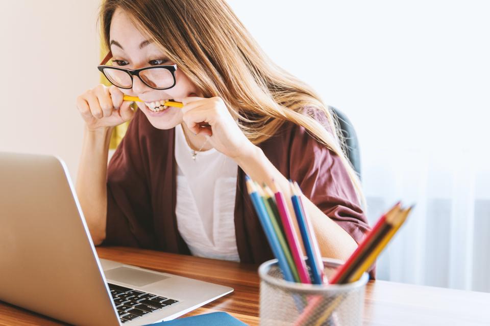 girl biting pencil in front of computer