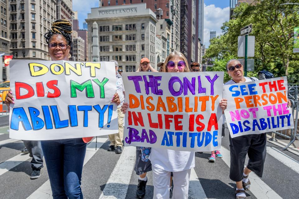 Photo of 3 people holding signs during the 5th Disability Pride March in New York.  It says on the signs 