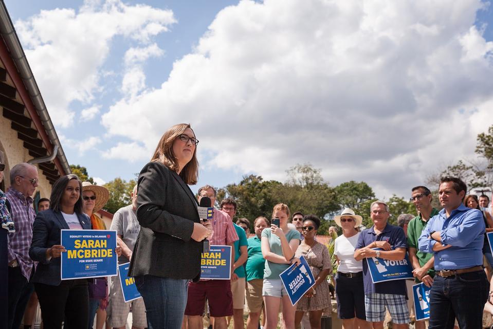 A woman stands in front of a group of people holding signs that say, 'Sarah McBride.'