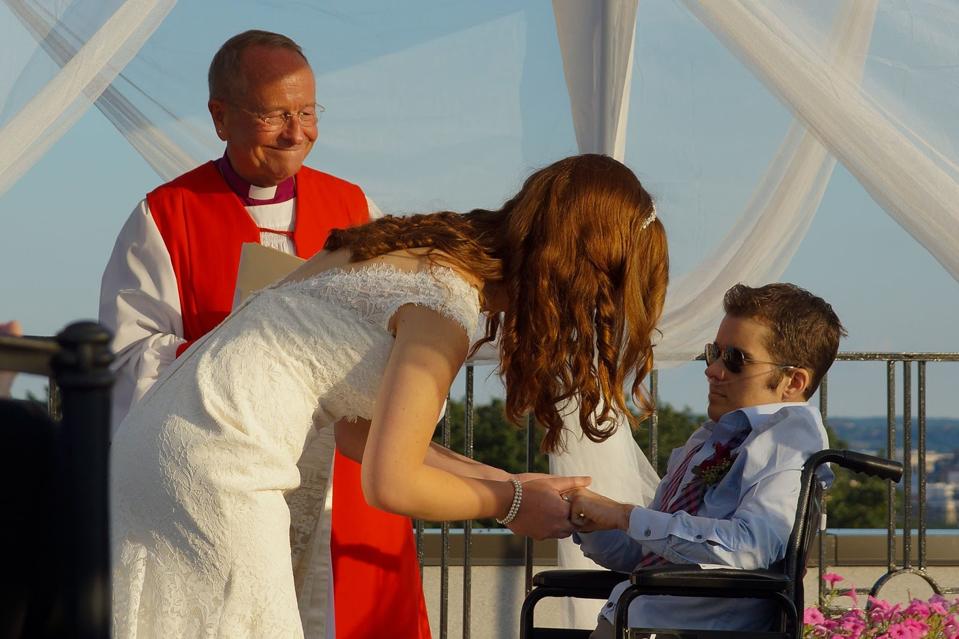 A woman in a wedding dress and a man in a wheelchair get married.
