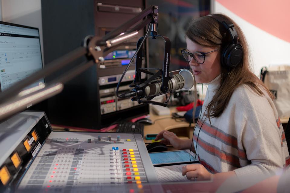 A young woman talks into a microphone in a radio studio.
