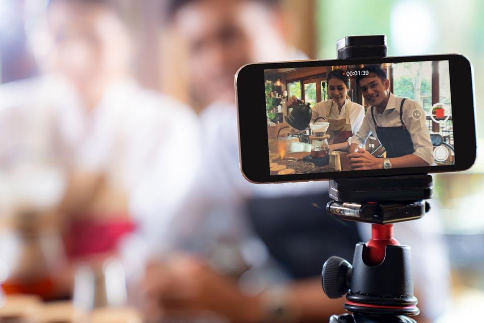 Young coffee shop owner recording a demonstration with their smartphone for a social media campaign.