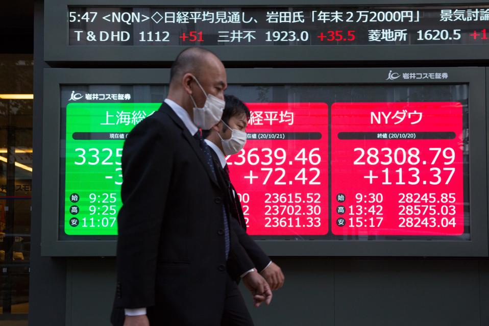 Men walking by an electronic stock exchange board with...