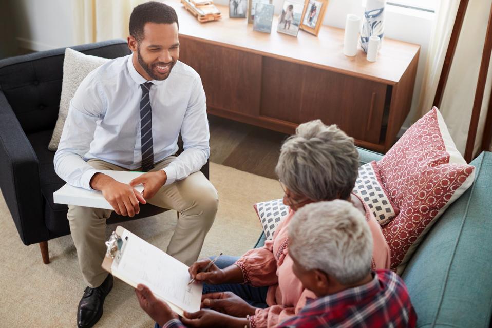 Senior Couple Meeting With Male Financial Advisor At Home And Signing Document