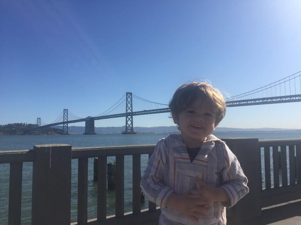 Elijah at the Ferry Building in San Francisco, with the Bay Bridge behind.