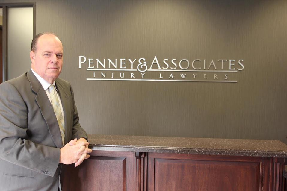 Middle-aged man in a suit in front of a Penney & Associates Injury Lawyers logo