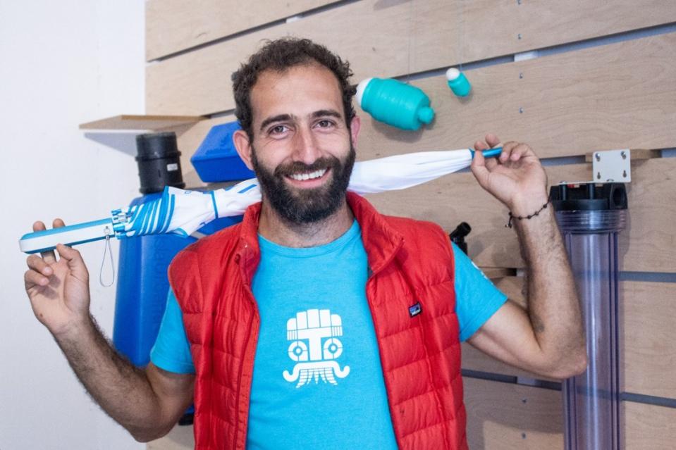 Photo of Enrique Lumnitz. He is a bearded white man holding an umbrella behind his back.