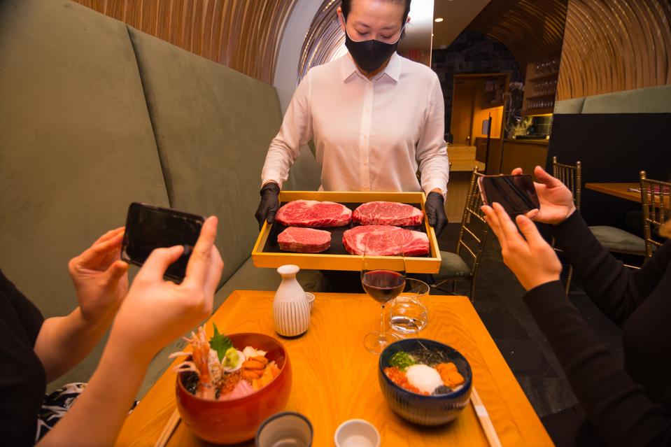 server at j-spec holding different wagyu steaks to diners with phones