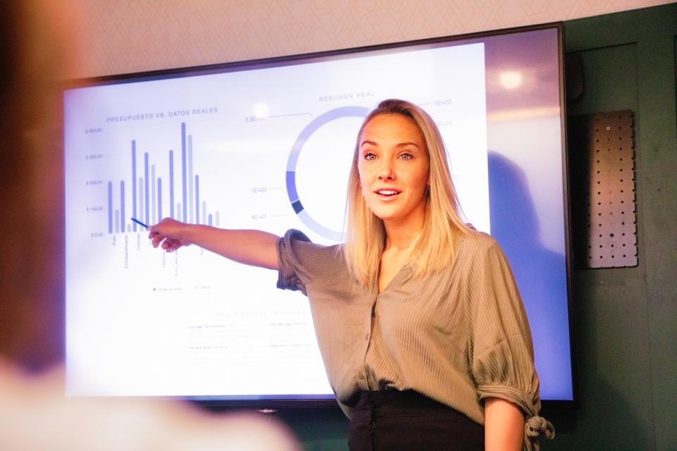Young blond female manager explaining quarterly results on large led screen