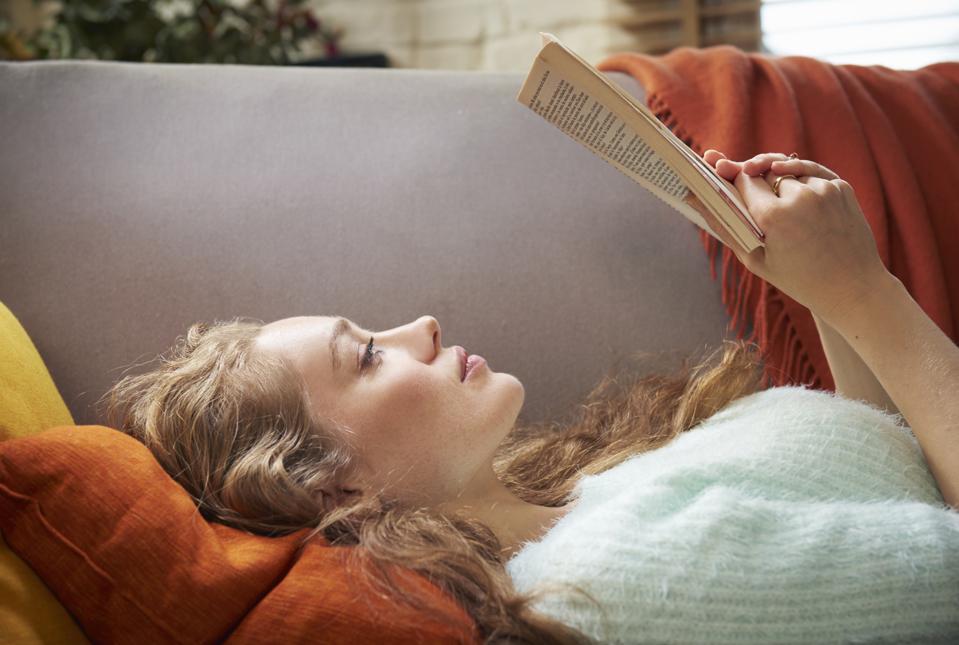 Young woman lying on sofa reading
