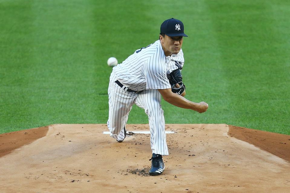 Right-handed Yankees pitcher Masahiro Tanaka is throwing a pitch towards home plate.