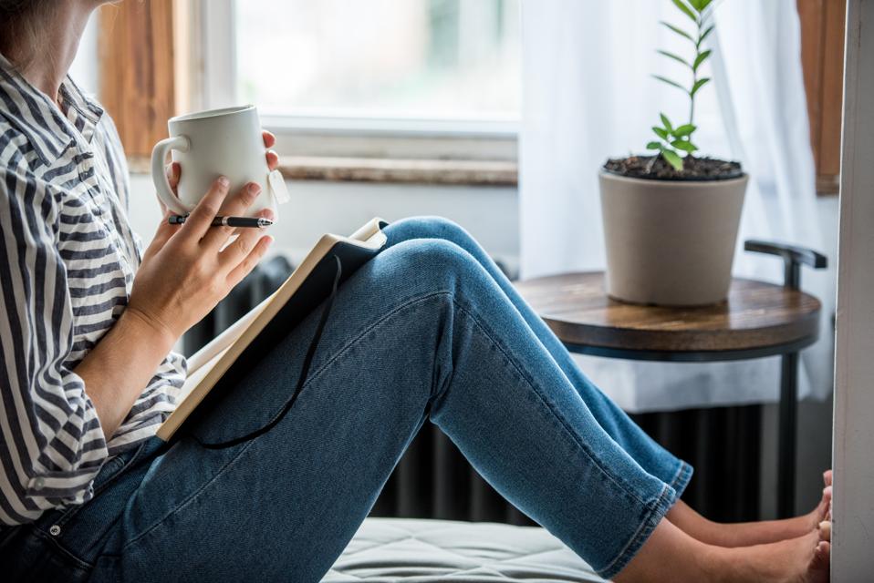 A young woman taking a break from technology with a cup of tea and a journal.