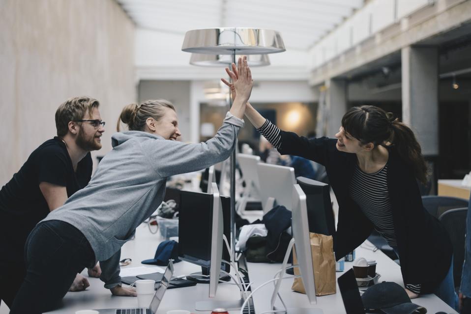 Happy female computer programmers giving high-five over desk in office