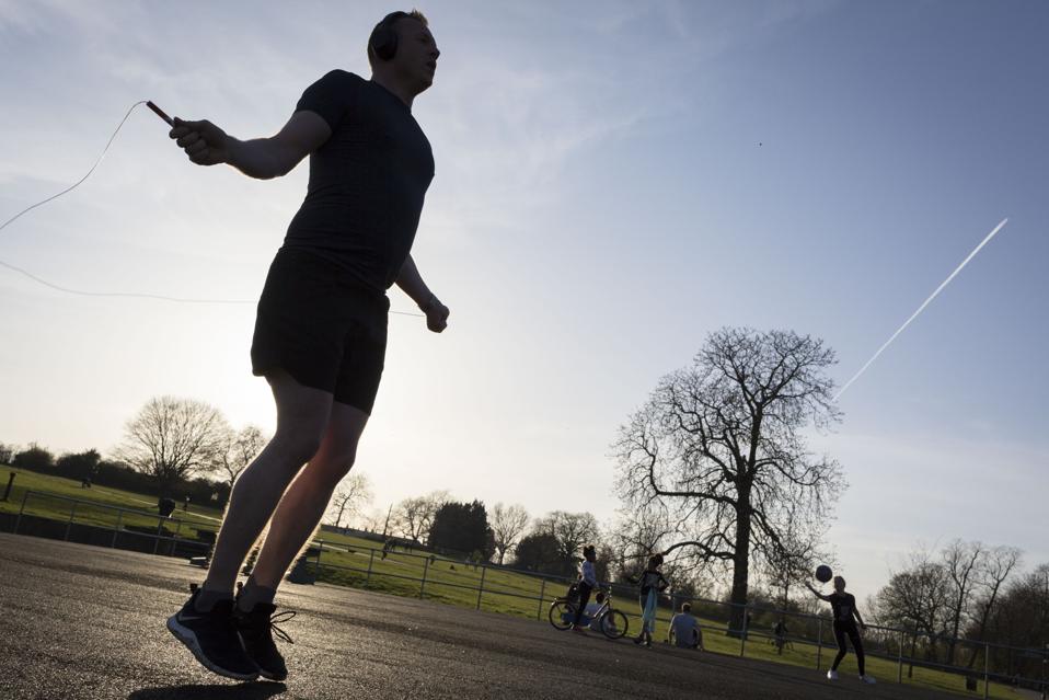 A man jumps rope under a blue sky in a London park.