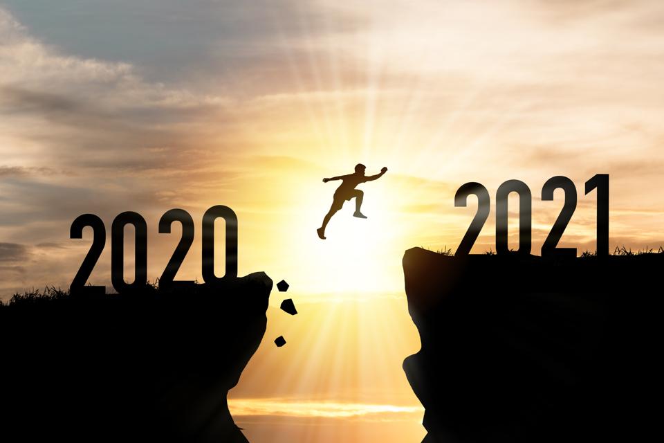 Person jumping from 2020 cliff to 2021 cliff with cloud sky and sunlight.