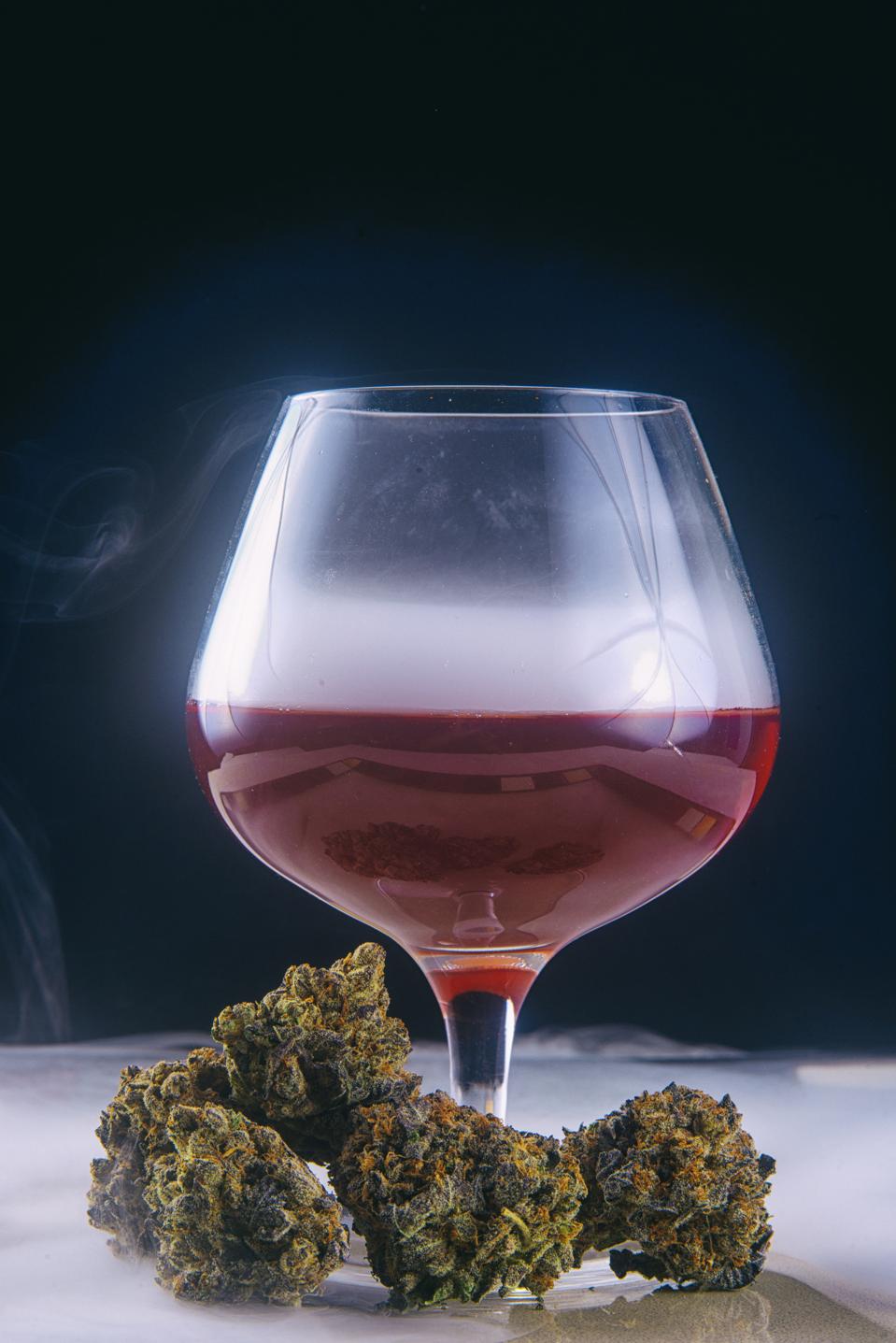 Dried cannabis buds (Grandaddy Purple strain) with glass of red wine isolated on black blackground.