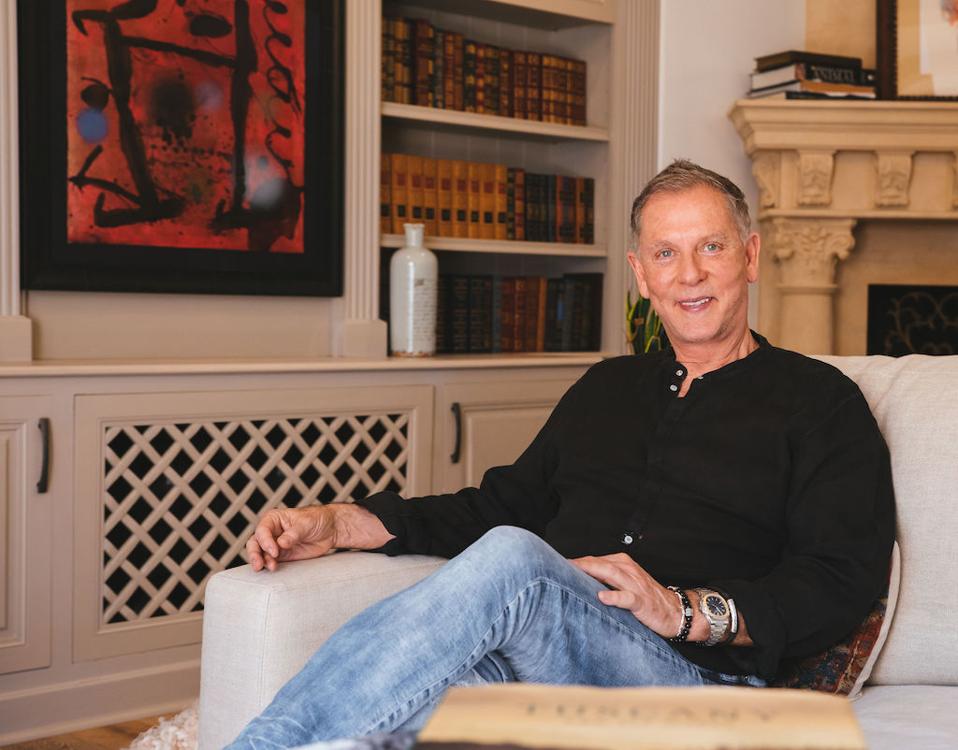 Man sitting in a study with bookshelves and art behind him