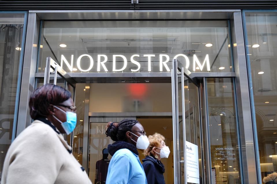 People wearing face masks walk past a Nordstrom Department...