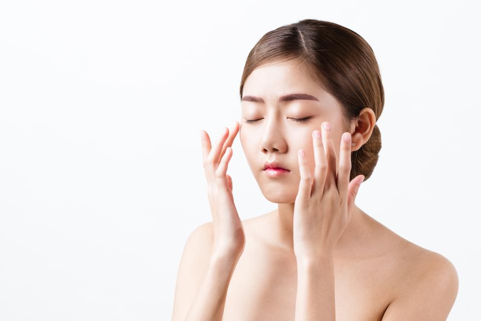 Portrait of beautiful healthy Asian woman close her eyes and massage her face gently with fingers, concept facial massage, cosmetology spa and beauty, isolated on white background with copy space