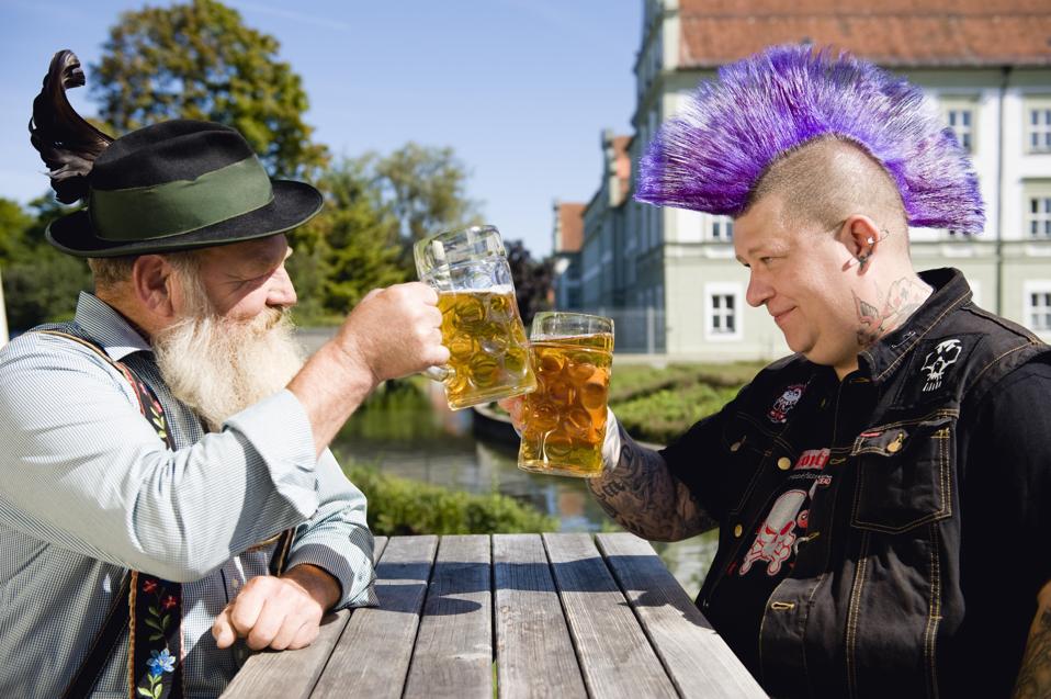 Germany, Bavaria, Upper Bavaria, Man with mohawk hairstyle and Bavarian man holding beer stein glasses
