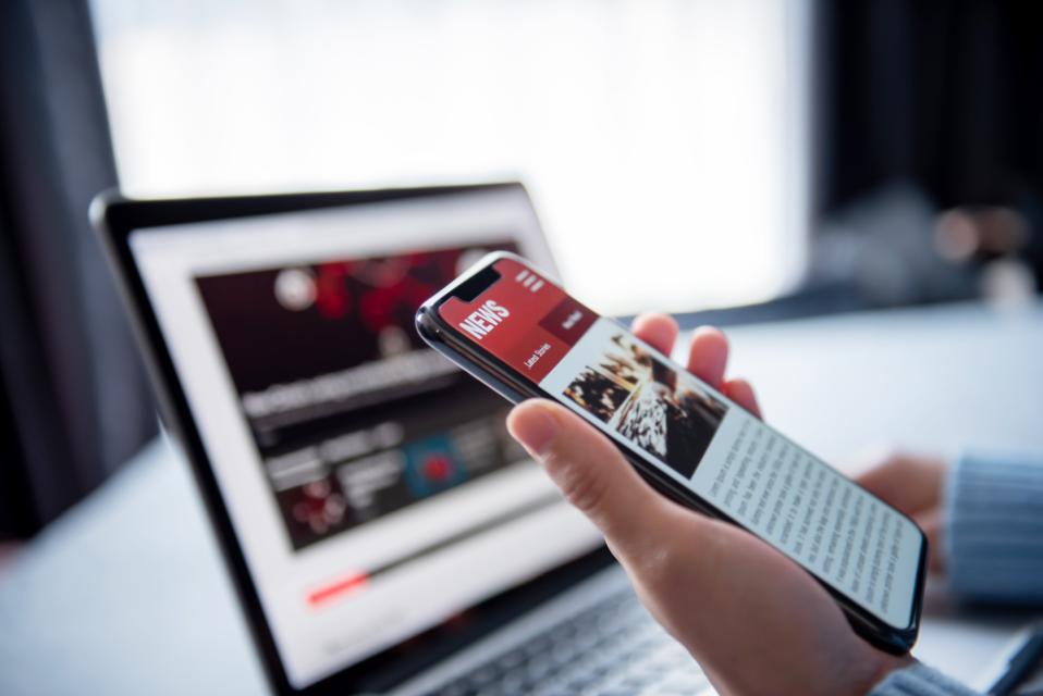 Person looking at the news on a smartphone and laptop. 