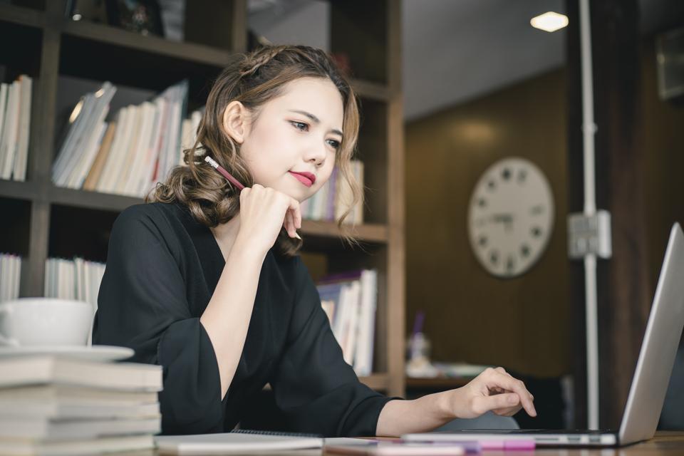 Low Angle View Of Businesswoman Using Laptop On Desk While Sitting Against Window In Office