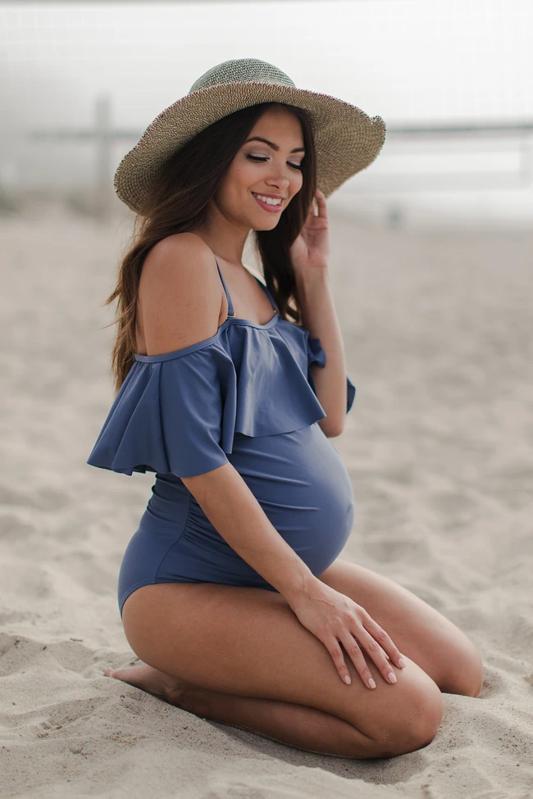 Model in blauw badpak met ruches op het strand.