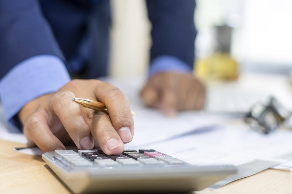 Close up Businessman using pen and calculator working on wooden desk