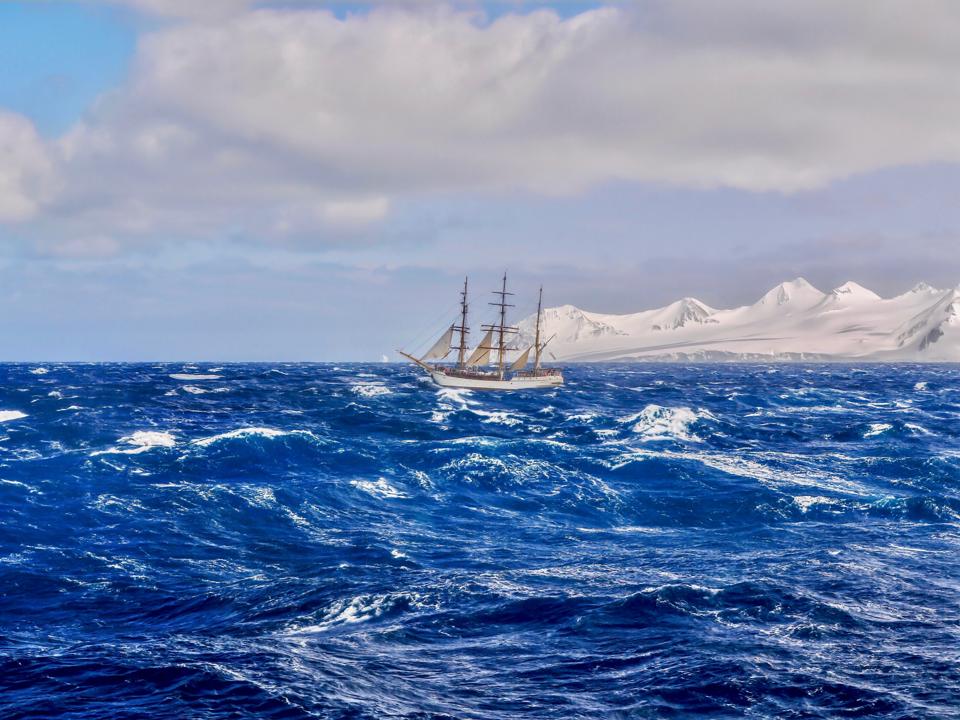 A traditional tall ship with reefed sails, sailing through rough seas in the southern Pacific Ocean.
