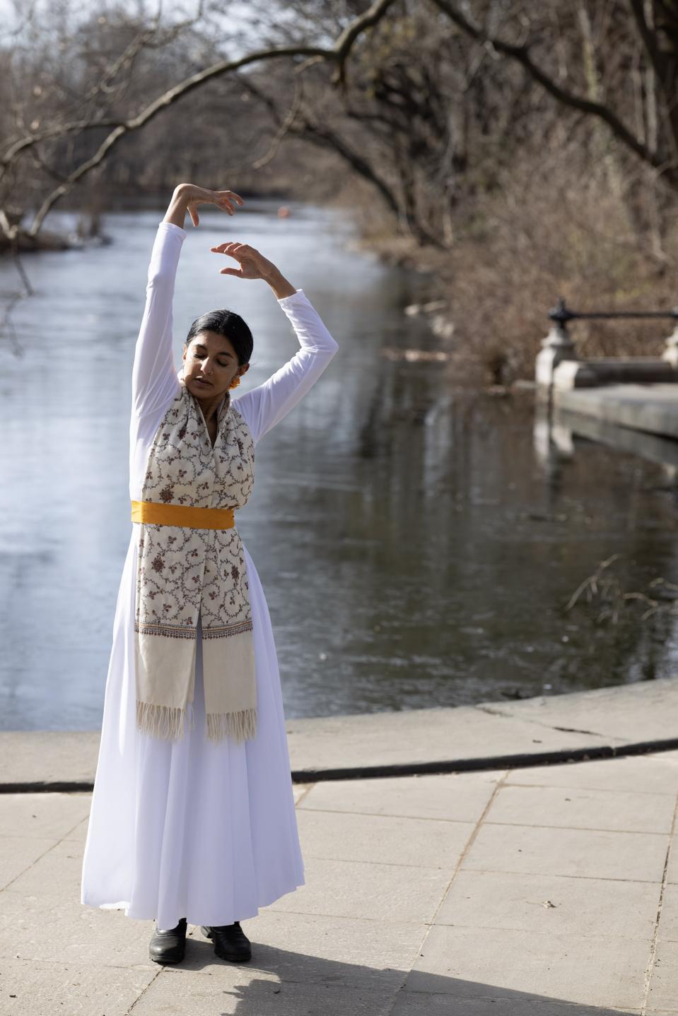 A woman in a white dress dances in front of a lake.