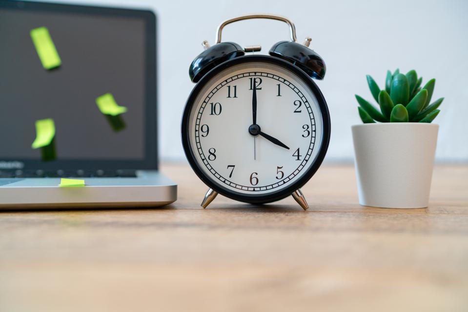 Alarm clock, laptop with postit notes and plant showing work-from-home productivity isn't what you thought.