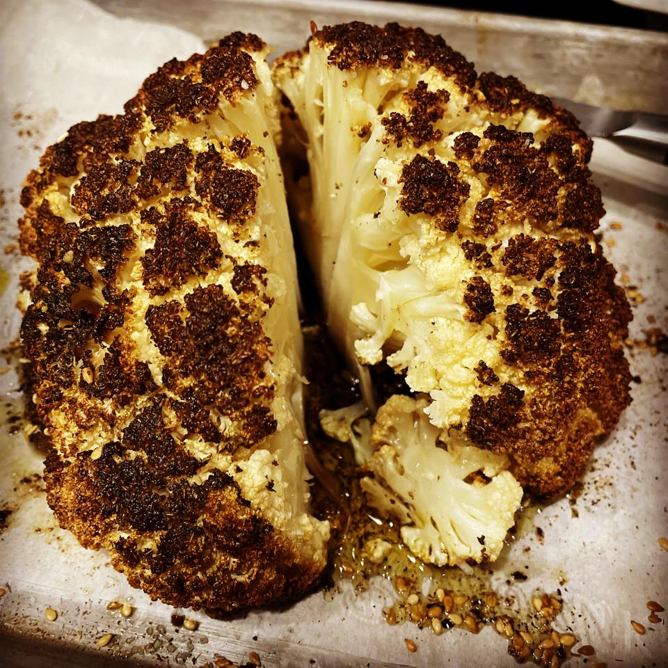 This roasted whole cauliflower is cut in half to show how tender the inside is and how caramelized and golden-brown the outside is. The head of cauliflower is coated with oil, seasoned and roasted while for 90 minutes.