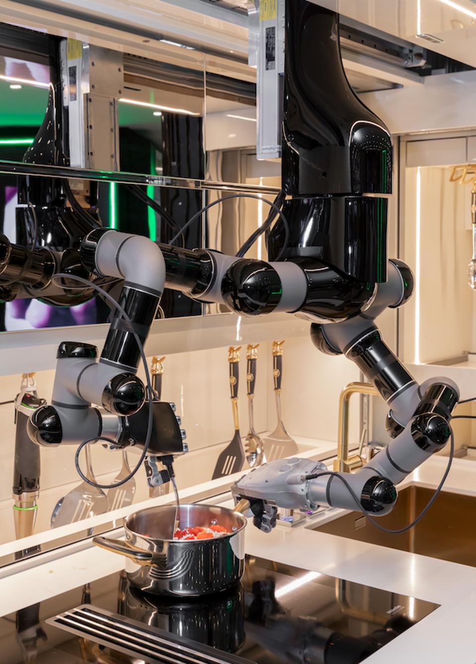 Robot stirs ingredients in a pan on an induction stove top.