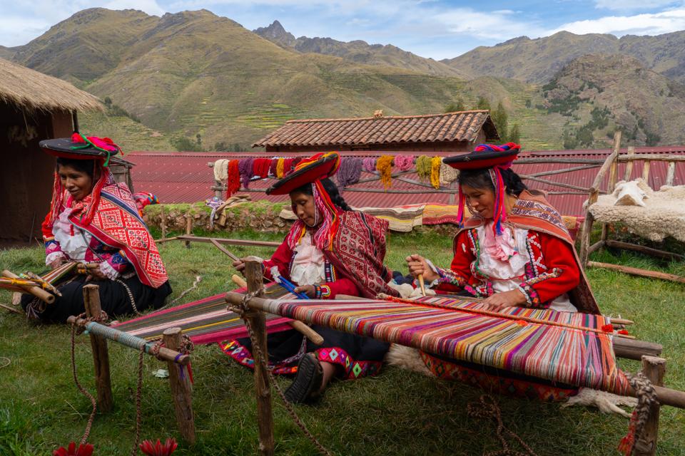 Three local Peruvian female weavers csitting on the ground, reating colourful alpaca wool in the Sacred Valley.l Releases and Property Release)