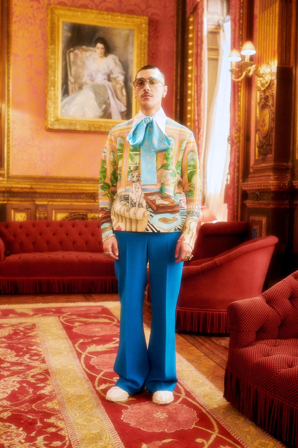 A male model wearing a colorful sweater with a bow and blue pants from the Casablanca ″Grand Prix.″collection.