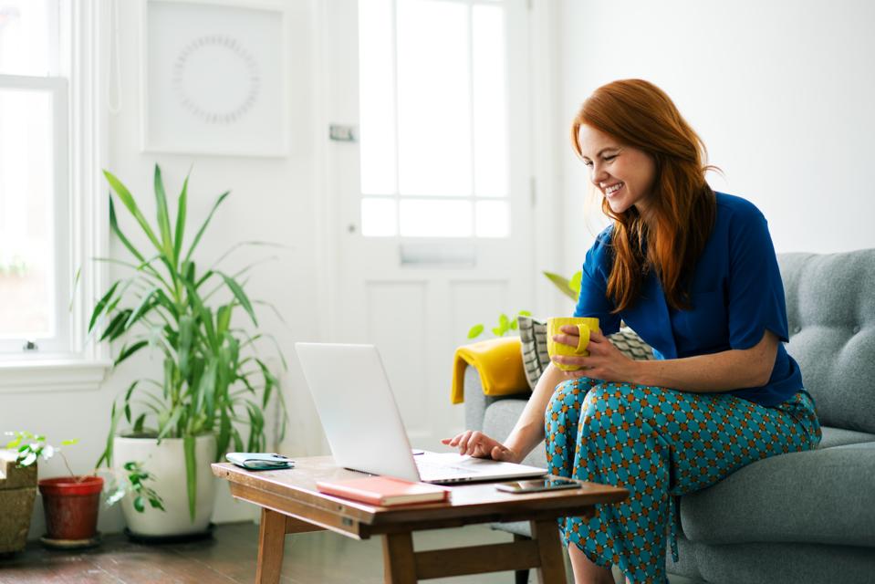 Woman using laptop from sofa, smiling