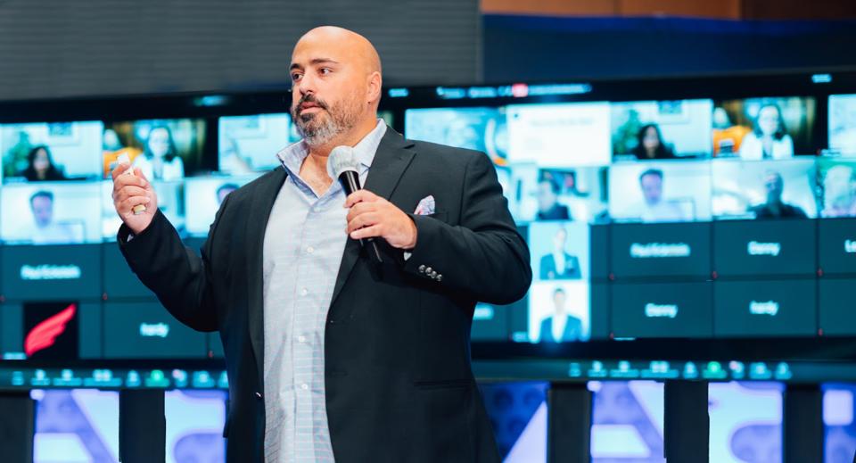 Man standing in front of screen with microphone giving keynote speech