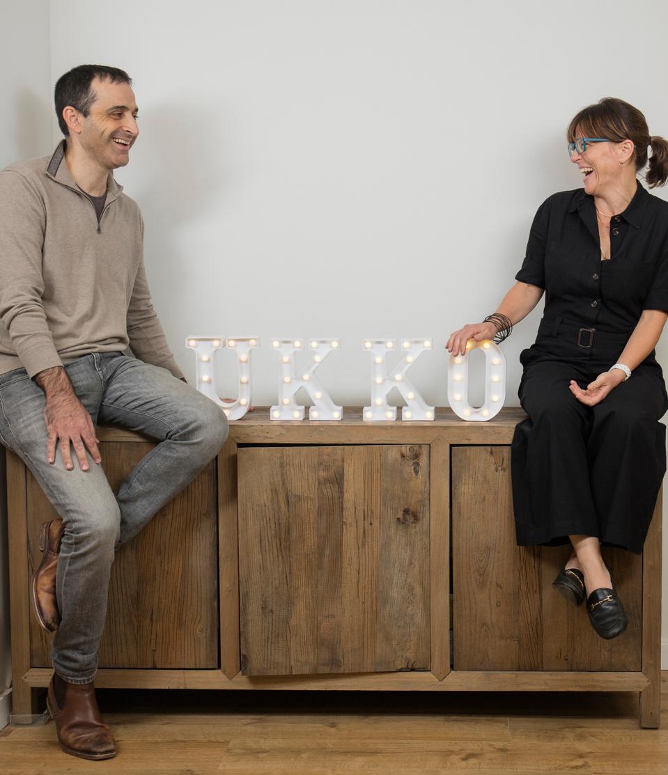 Un homme blanc et une femme blanche assis sur une crédence en bois riant l'un de l'autre.