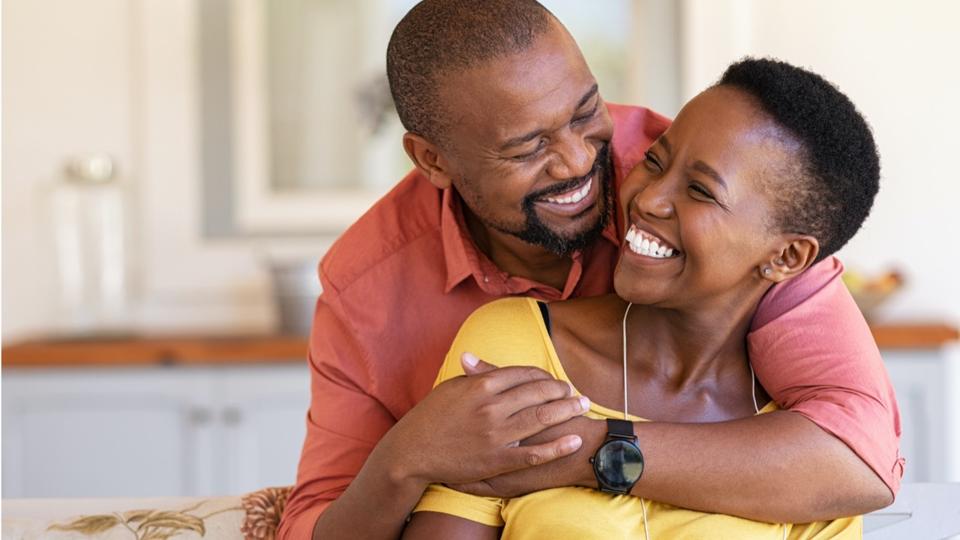 A happy couple, a smiling man with arms around a smiling woman, sharing a joyous moment.
