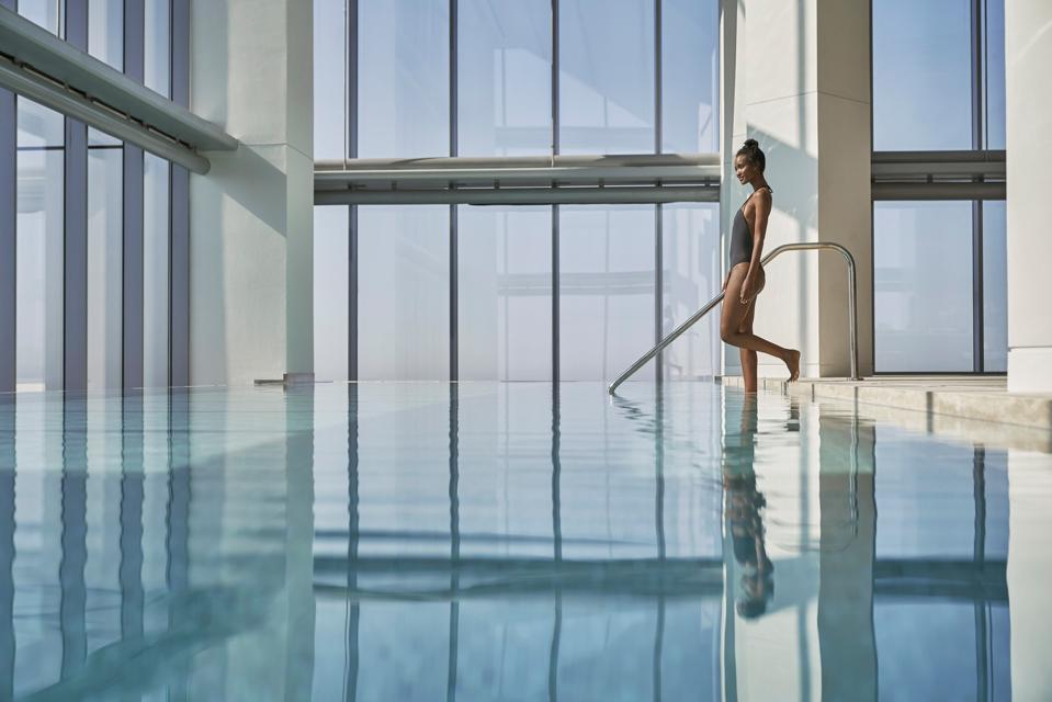 A woman in a one-piece bathing suit steps into the pool at Four Seasons Philadelphia