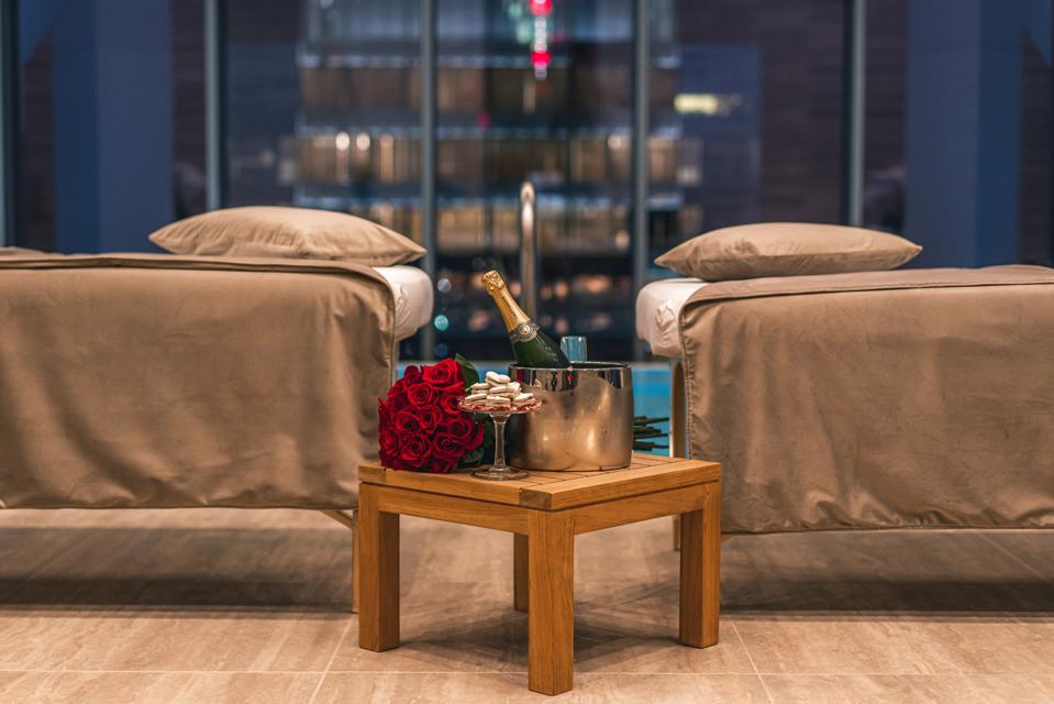 Two massage chairs are separated by a side table supporting champagne and roses.